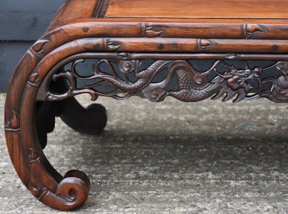 An antique Chinese rosewood low coffee table featuring elaborate openwork dragon carvings on the apron and curved scroll legs with bamboo motif borders. View III