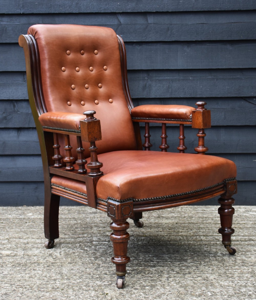 A 19th-century mahogany library armchair featuring warm brown button-tufted leather upholstery, turned spindle arm supports, and turned front legs on brass castors. View II