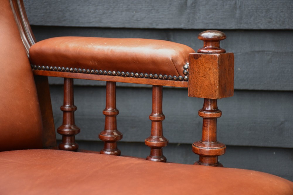 A 19th-century mahogany library armchair featuring warm brown button-tufted leather upholstery, turned spindle arm supports, and turned front legs on brass castors. View IV