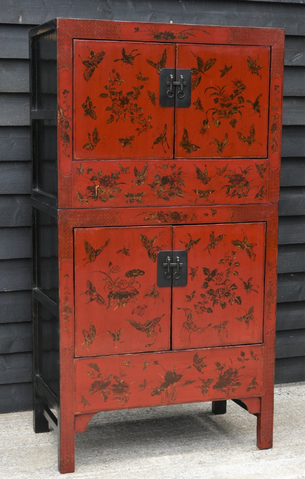 A two-tier red lacquered Chinese cabinet featuring hand-painted floral and butterfly details with black frame framing and dark metal door hardware.