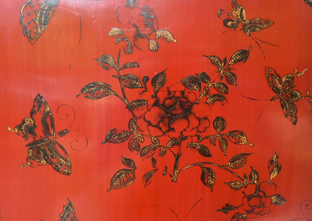 A two-tier red lacquered Chinese cabinet featuring hand-painted floral and butterfly details with black frame framing and dark metal door hardware. View III