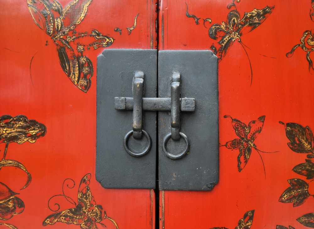 A two-tier red lacquered Chinese cabinet featuring hand-painted floral and butterfly details with black frame framing and dark metal door hardware. View IV