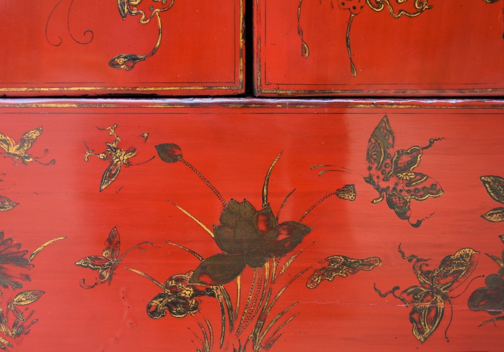 A two-tier red lacquered Chinese cabinet featuring hand-painted floral and butterfly details with black frame framing and dark metal door hardware. View V
