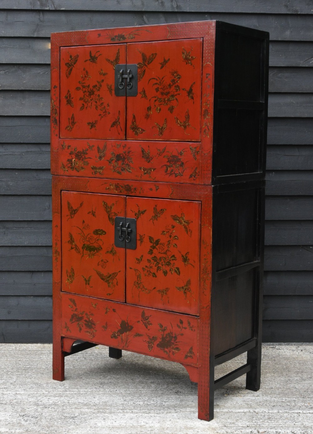 A two-tier red lacquered Chinese cabinet featuring hand-painted floral and butterfly details with black frame framing and dark metal door hardware. View VI