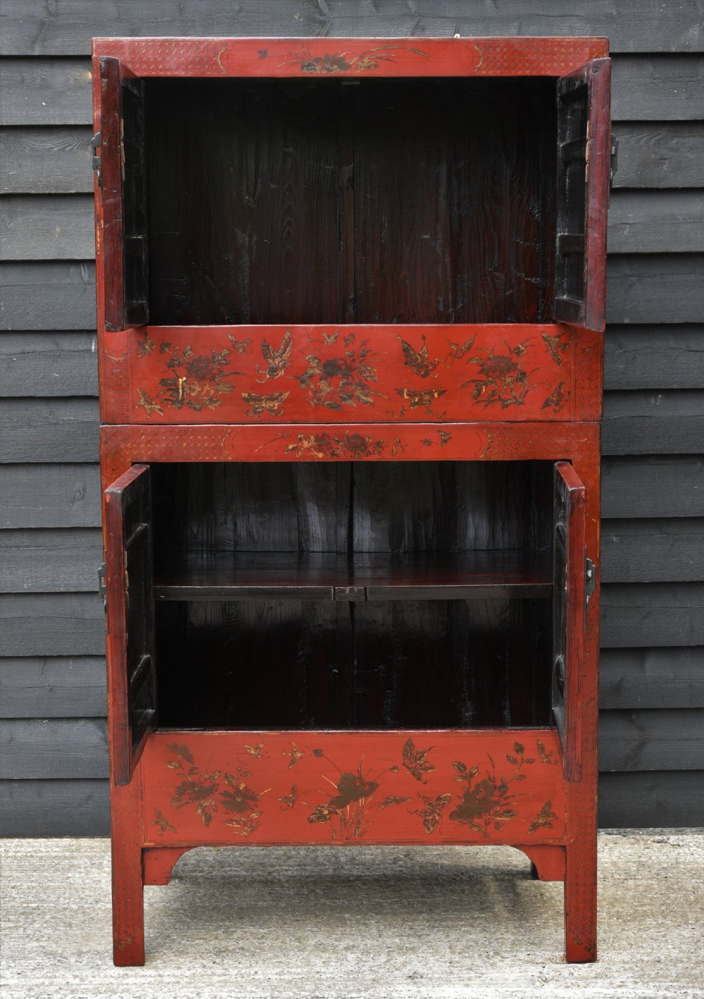 A two-tier red lacquered Chinese cabinet featuring hand-painted floral and butterfly details with black frame framing and dark metal door hardware. View VII