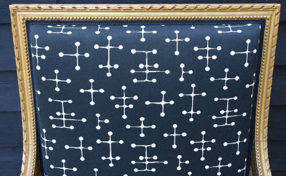 A French Louis XVI style giltwood open armchair upholstered in dark blue fabric with white geometric motifs, featuring fluted legs and carved leaf moulding. View V