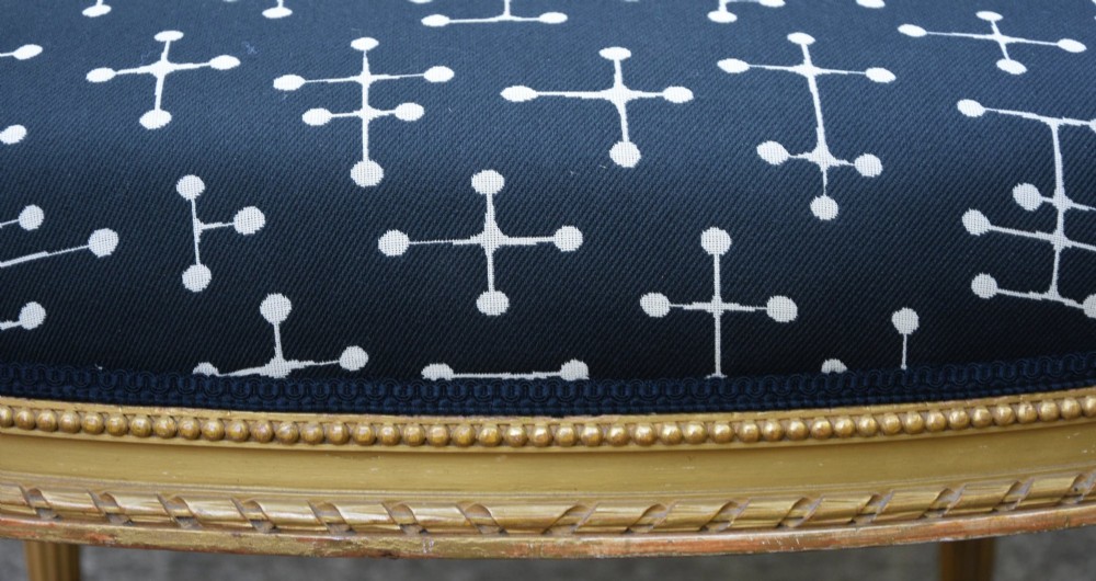 A French Louis XVI style giltwood open armchair upholstered in dark blue fabric with white geometric motifs, featuring fluted legs and carved leaf moulding. View VI