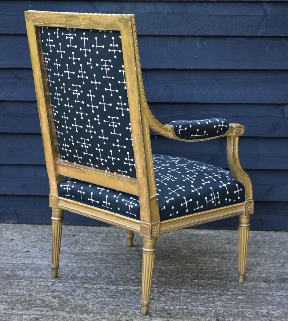 A French Louis XVI style giltwood open armchair upholstered in dark blue fabric with white geometric motifs, featuring fluted legs and carved leaf moulding. View VII