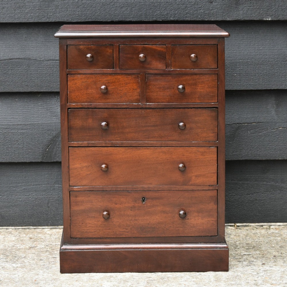A Victorian mahogany miniature chest featuring eight graduated drawers with turned wooden handles on a solid plinth base.