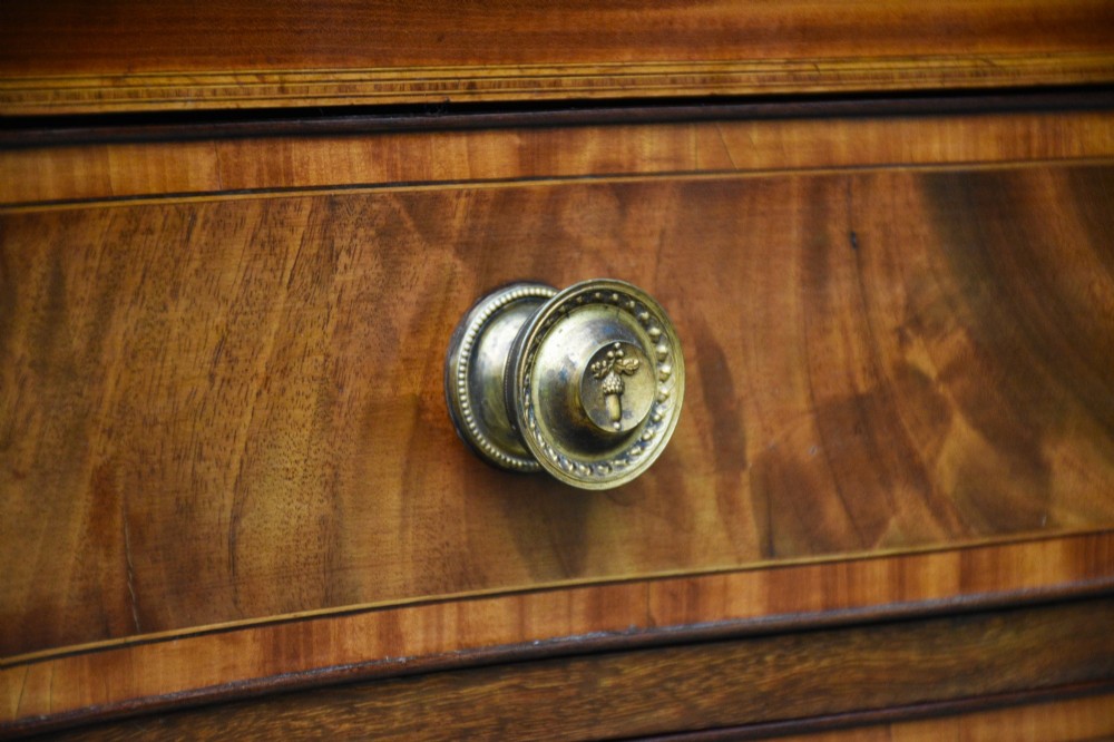 A late 18th-century Georgian serpentine chest of drawers crafted from flame mahogany with satinwood crossbanding, four graduated drawers, brass knobs, and bracket feet. View III