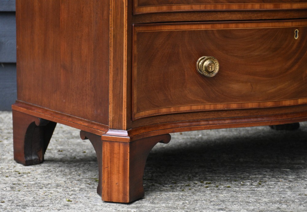 A late 18th-century Georgian serpentine chest of drawers crafted from flame mahogany with satinwood crossbanding, four graduated drawers, brass knobs, and bracket feet. View IV