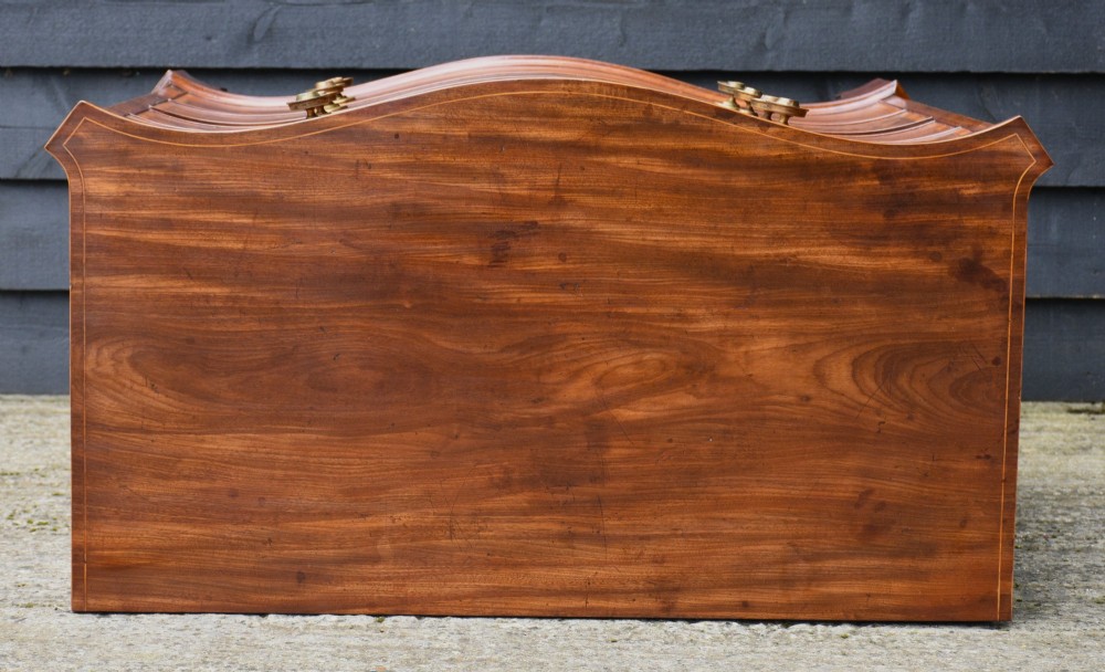 A late 18th-century Georgian serpentine chest of drawers crafted from flame mahogany with satinwood crossbanding, four graduated drawers, brass knobs, and bracket feet. View XI
