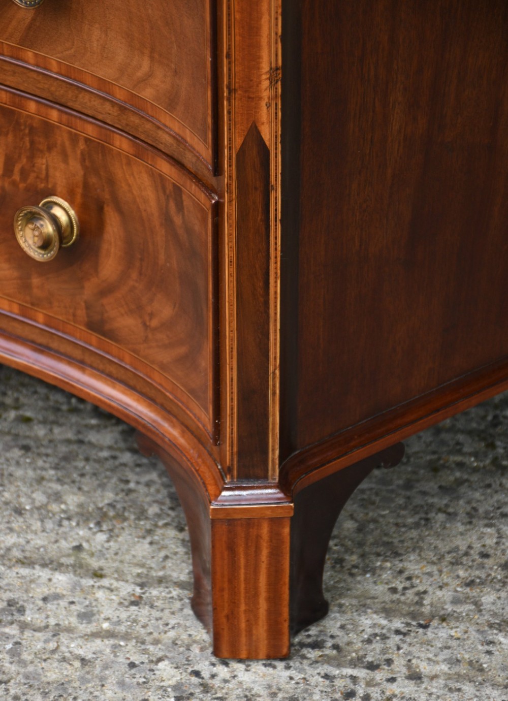 A late 18th-century Georgian serpentine chest of drawers crafted from flame mahogany with satinwood crossbanding, four graduated drawers, brass knobs, and bracket feet. View XII