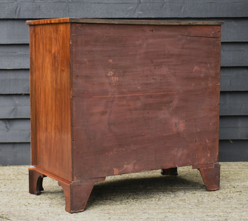 A late 18th-century Georgian serpentine chest of drawers crafted from flame mahogany with satinwood crossbanding, four graduated drawers, brass knobs, and bracket feet. View XIII