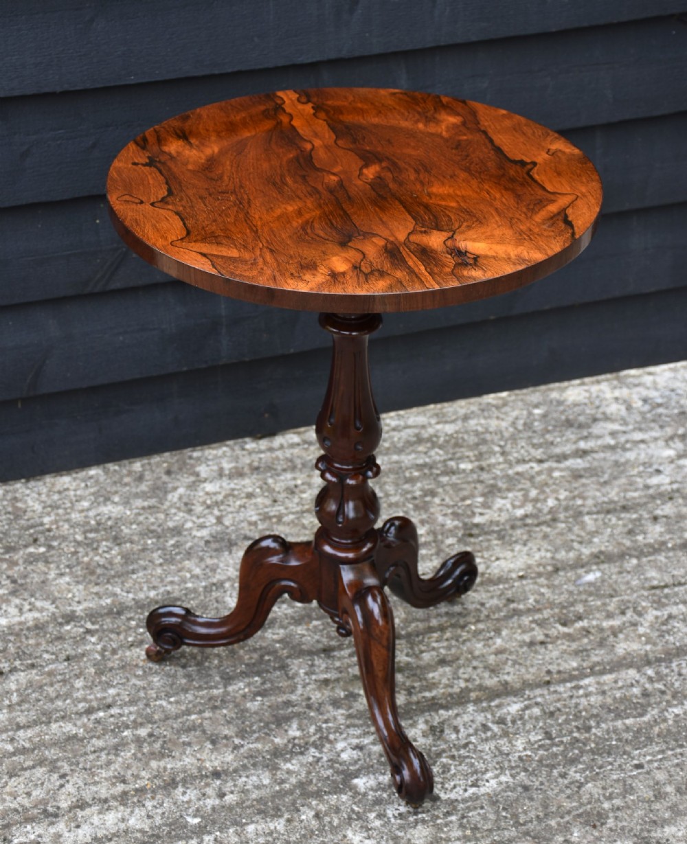 A 19th-century rosewood wine table with a figured circular top, turned central pedestal, and carved tripod scroll legs.