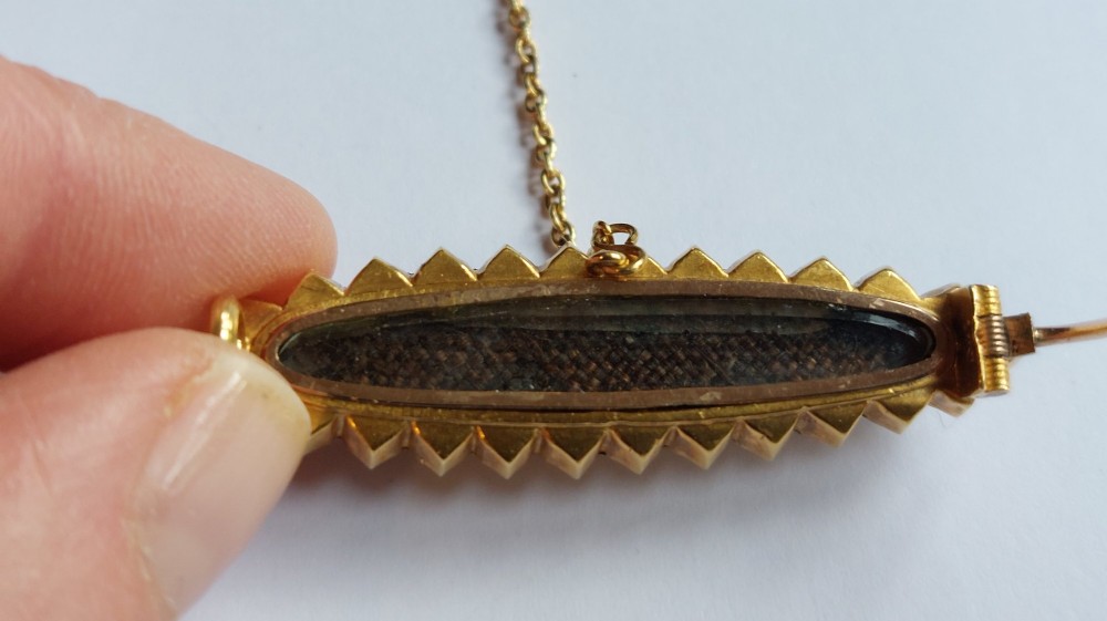 An elongated Victorian navette-shaped gold brooch featuring a central black onyx plaque with a starburst-set seed pearl, surrounded by a outer border of seed pearls. View III