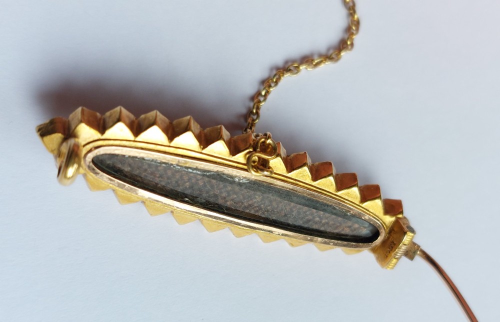 An elongated Victorian navette-shaped gold brooch featuring a central black onyx plaque with a starburst-set seed pearl, surrounded by a outer border of seed pearls. View V