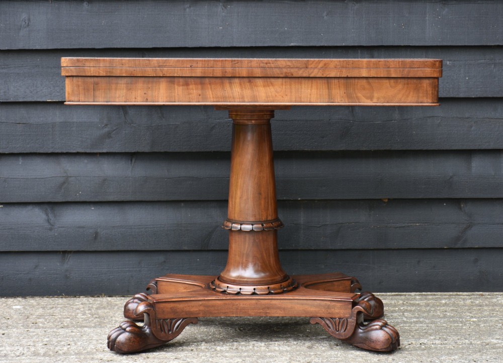 A 19th-century William IV mahogany card table featuring a fold-over top, a cylindrical pedestal column, and a shaped quadripartite base with carved claw feet.