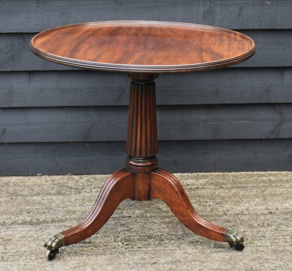 A Regency mahogany tripod tea table featuring a circular revolving top, a fluted pedestal stem, and three downswept reeded legs with brass claw castors.