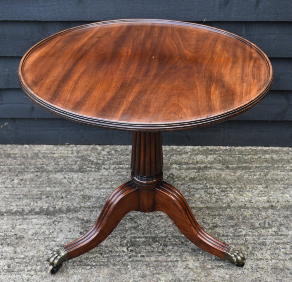 A Regency mahogany tripod tea table featuring a circular revolving top, a fluted pedestal stem, and three downswept reeded legs with brass claw castors. View III