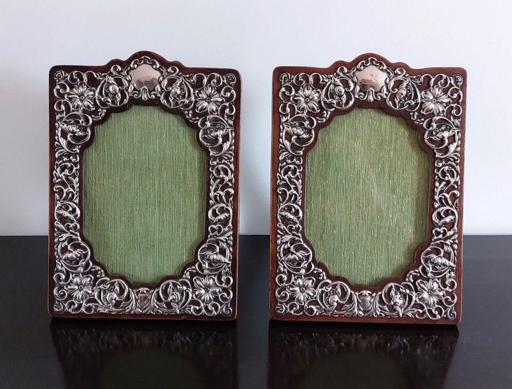 A pair of ornate Edwardian silver photograph frames featuring detailed foliate repousse borders on dark wood backs with green textured centres.