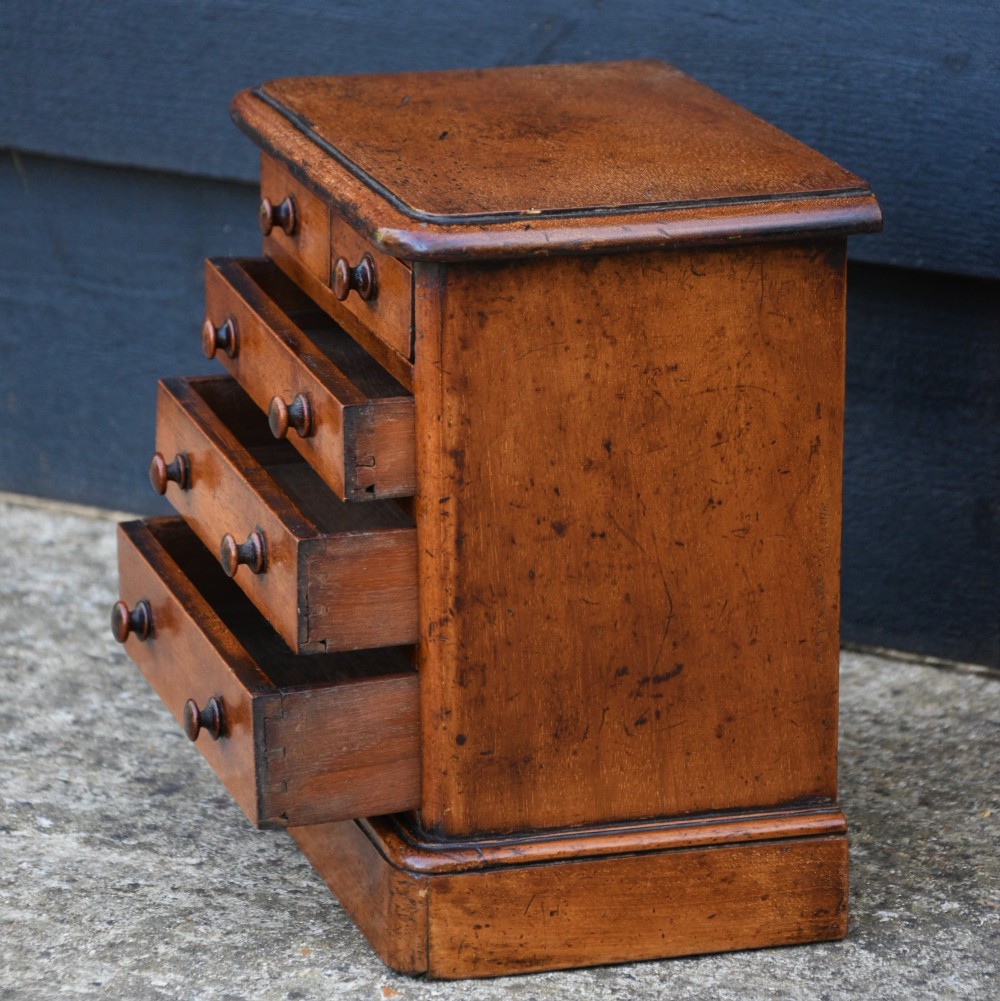 A Victorian mahogany miniature chest of drawers featuring two short over three long drawers with turned knobs on a plinth base. View VI