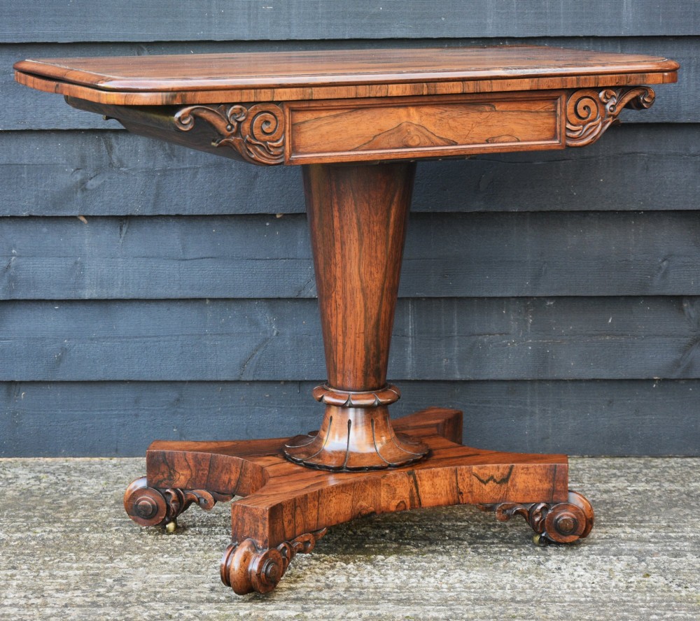 A 19th-century William IV rosewood tea table featuring a rectangular fold-over top, carved scroll apron, a central tapered pedestal, and a shaped quadform base with scroll feet. View II