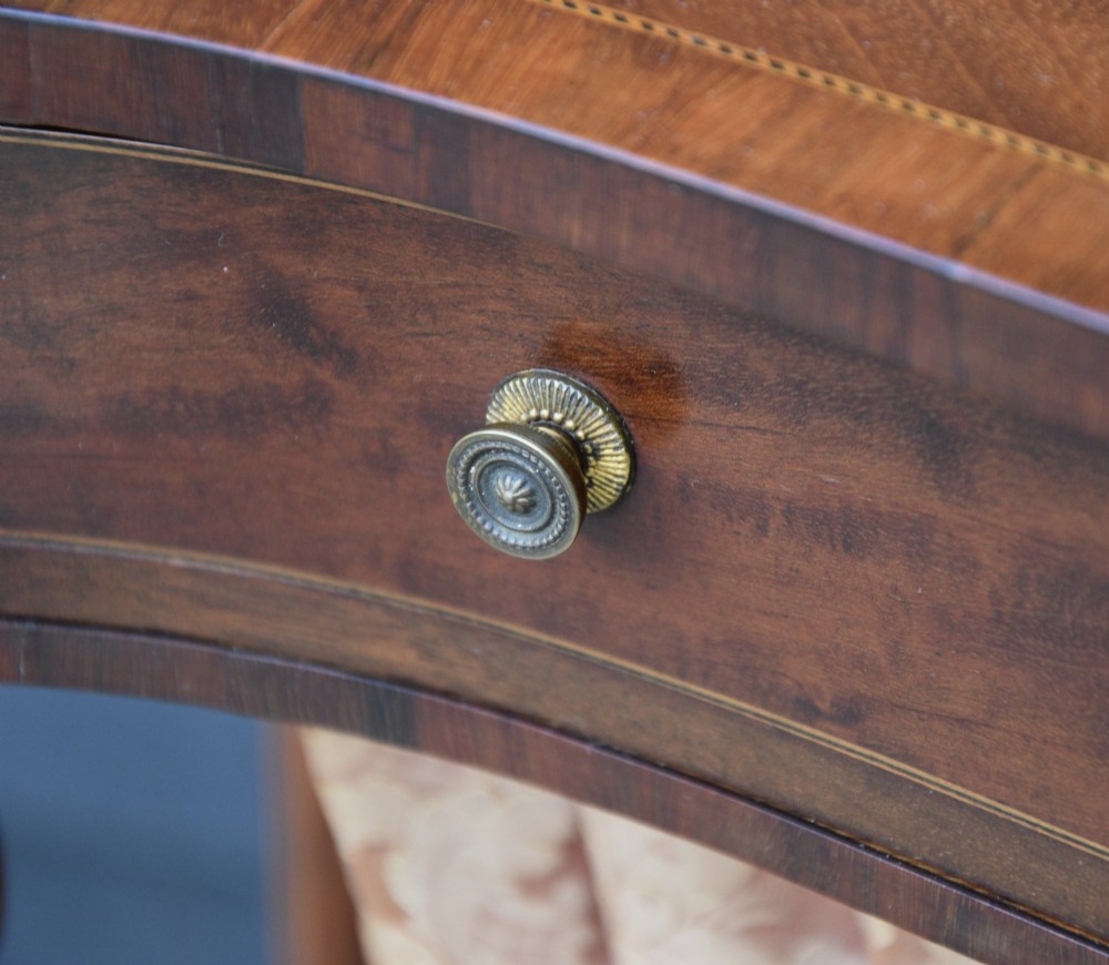 An Edwardian mahogany sewing table featuring a serpentine front, turned legs, an X-stretcher, and a pleated fabric pouch underneath. View V