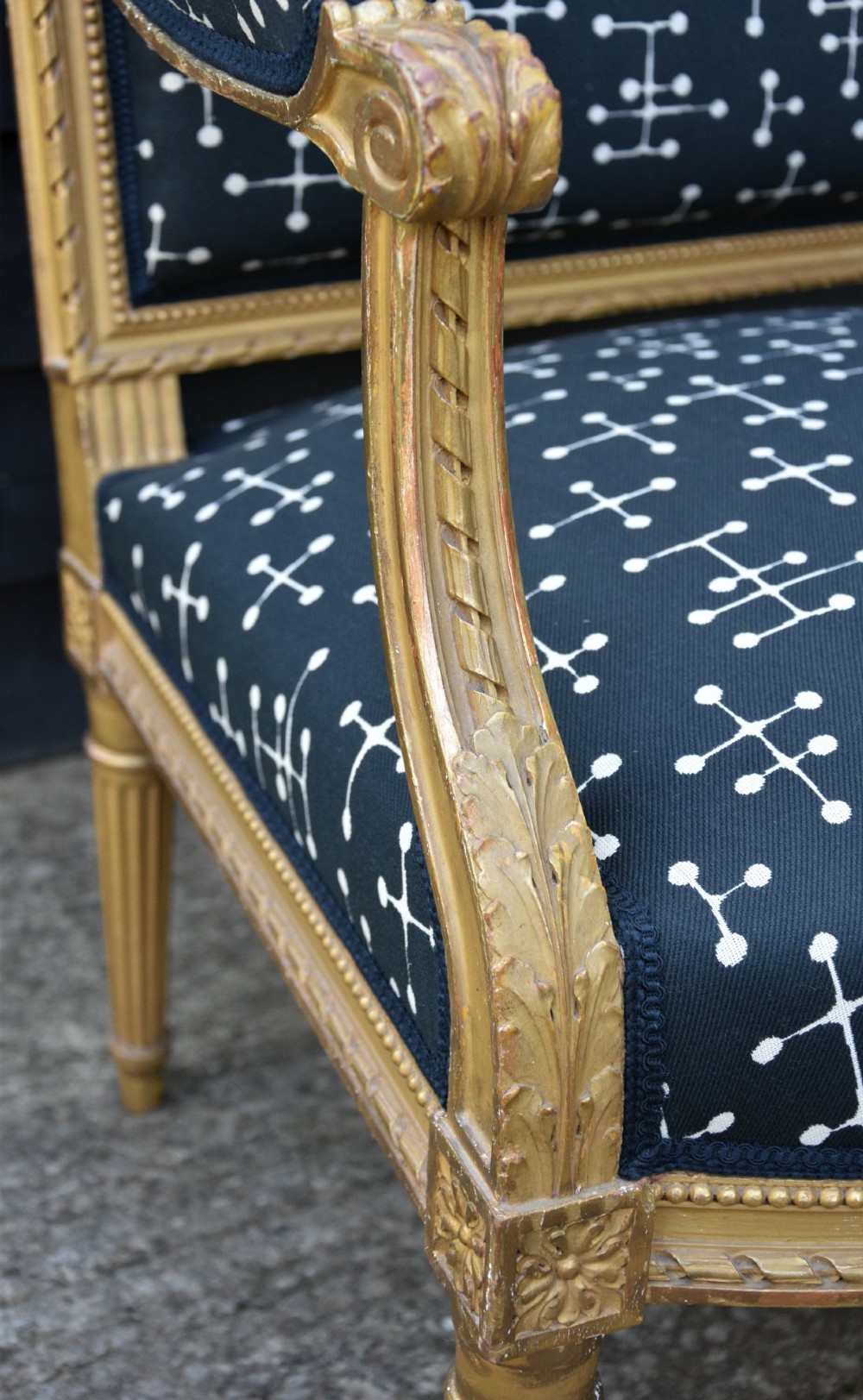 A French Louis XVI style open armchair featuring a carved gold-leaf frame with fluted legs and dark navy fabric upholstery adorned with a white geometric pattern. View VII