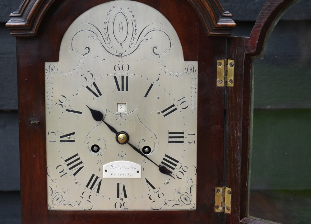 A Georgian mahogany bracket clock featuring an arched wooden case, brass top handle, fluted brass feet, and an engraved dial with Roman numerals. View IV