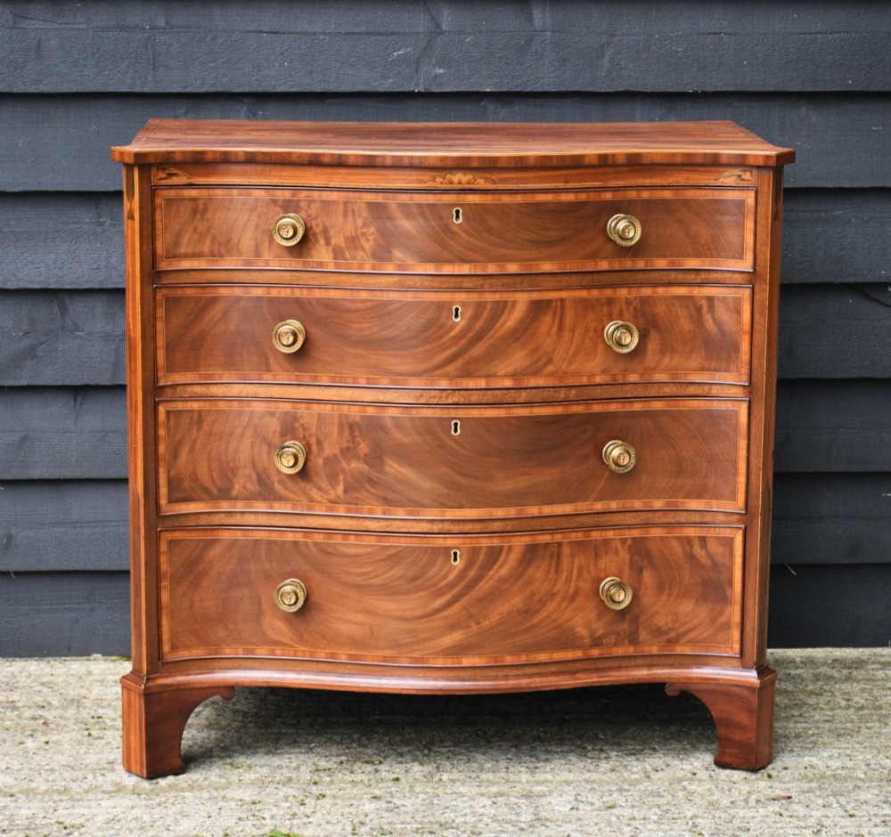 A late 18th-century Georgian serpentine mahogany chest of drawers featuring four graduated drawers, brass handles, inlay details, and shaped bracket feet. View XIV