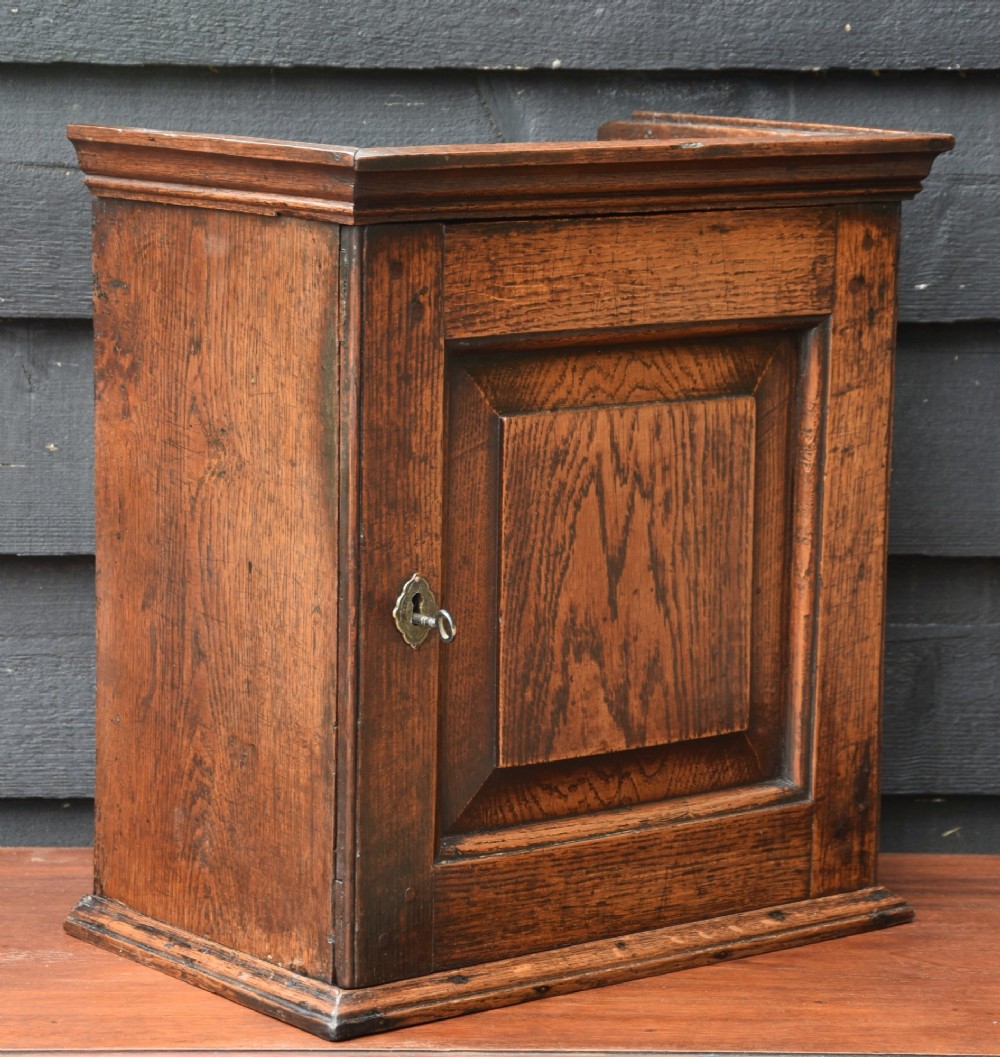 An early eighteenth-century oak spice cupboard featuring a single fielded panel door with a brass escutcheon and key, set on a moulded base.