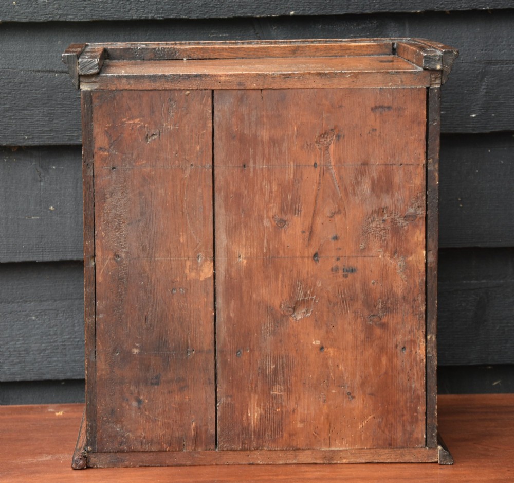 An early eighteenth-century oak spice cupboard featuring a single fielded panel door with a brass escutcheon and key, set on a moulded base. View VIII