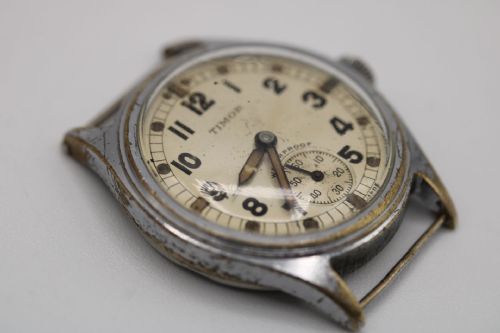 fig 1. A vintage Timor ATP military wristwatch featuring a round cream dial, black Arabic numerals, a sub-seconds subdial, and a weathered chrome-plated case.