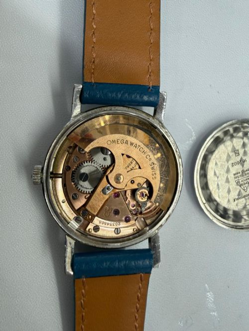 fig 2. A 1963 stainless steel Omega Seamaster automatic wrist watch featuring a silver dial with baton indices, date window at three oclock, and a blue leather strap.