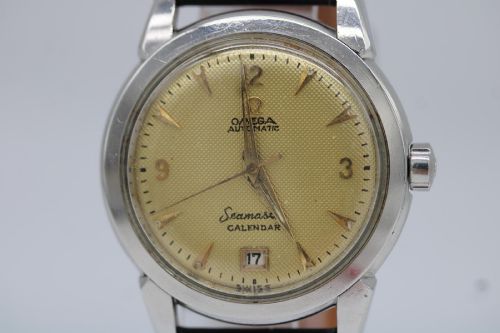 fig 5. A vintage 1952 Omega Seamaster Calendar wristwatch featuring a stainless steel case, textured gold-coloured dial with date display at six oclock, and a black leather strap.