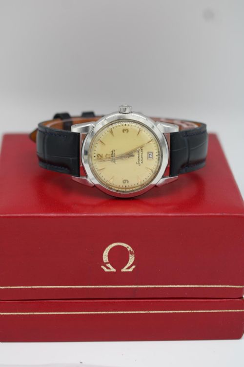 fig 6. A vintage 1952 Omega Seamaster Calendar wristwatch featuring a stainless steel case, textured gold-coloured dial with date display at six oclock, and a black leather strap.