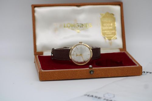 fig 1. A vintage circular 9ct gold wristwatch by Longines featuring a silver dial with gold baton hour markers and a brown leather strap.