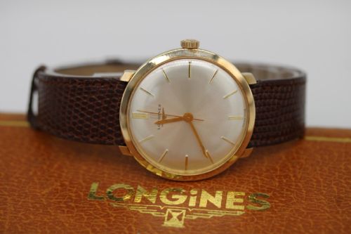 fig 2. A vintage circular 9ct gold wristwatch by Longines featuring a silver dial with gold baton hour markers and a brown leather strap.