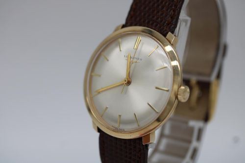 fig 4. A vintage circular 9ct gold wristwatch by Longines featuring a silver dial with gold baton hour markers and a brown leather strap.