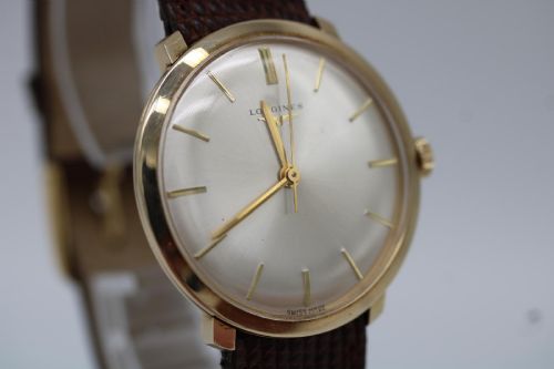 fig 6. A vintage circular 9ct gold wristwatch by Longines featuring a silver dial with gold baton hour markers and a brown leather strap.