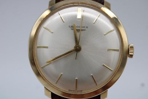 fig 7. A vintage circular 9ct gold wristwatch by Longines featuring a silver dial with gold baton hour markers and a brown leather strap.