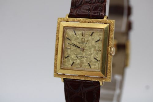 fig 4. A 1960s Omega Geneve manual wind wristwatch featuring an 18ct yellow gold cushion-shaped case, a dark brown dial with gold Roman numerals at twelve and six, and a brown leather strap.
