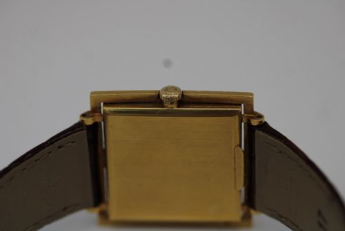 fig 7. A 1960s Omega Geneve manual wind wristwatch featuring an 18ct yellow gold cushion-shaped case, a dark brown dial with gold Roman numerals at twelve and six, and a brown leather strap.