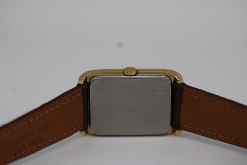 fig 8. A 1960s Omega Geneve manual wind wristwatch featuring an 18ct yellow gold cushion-shaped case, a dark brown dial with gold Roman numerals at twelve and six, and a brown leather strap.