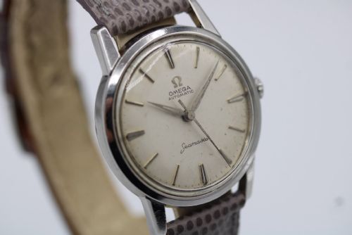 fig 3. A vintage 1960 Omega Seamaster automatic wristwatch with a stainless steel case, silver cream dial, and grey textured leather strap.