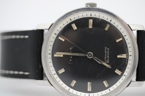 fig 1. A vintage Bulova automatic wristwatch featuring a black dial with silver baton hour markers and a black leather strap with white stitching.