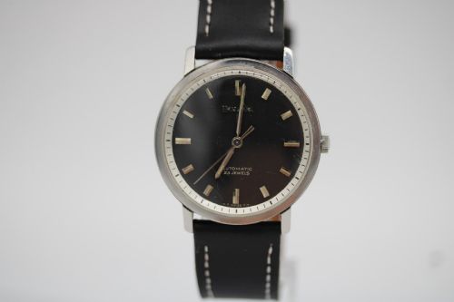 fig 2. A vintage Bulova automatic wristwatch featuring a black dial with silver baton hour markers and a black leather strap with white stitching.