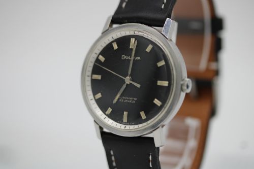 fig 3. A vintage Bulova automatic wristwatch featuring a black dial with silver baton hour markers and a black leather strap with white stitching.