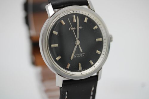 fig 4. A vintage Bulova automatic wristwatch featuring a black dial with silver baton hour markers and a black leather strap with white stitching.